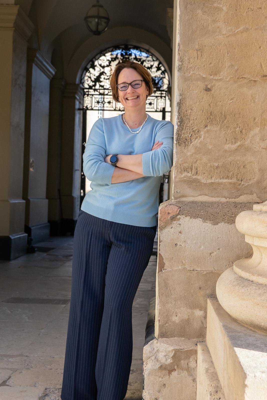 Portrait photograph, leaning against a stone column in a sunlit colonnade